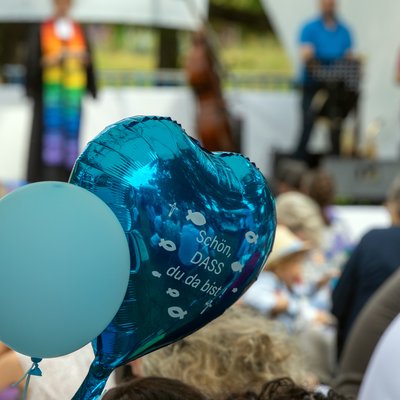 Zwei Luftballons beim "Main Tauffest 2022". Einer ist herzförmig und trägt die Aufschrift "Schön, dass du da bist".